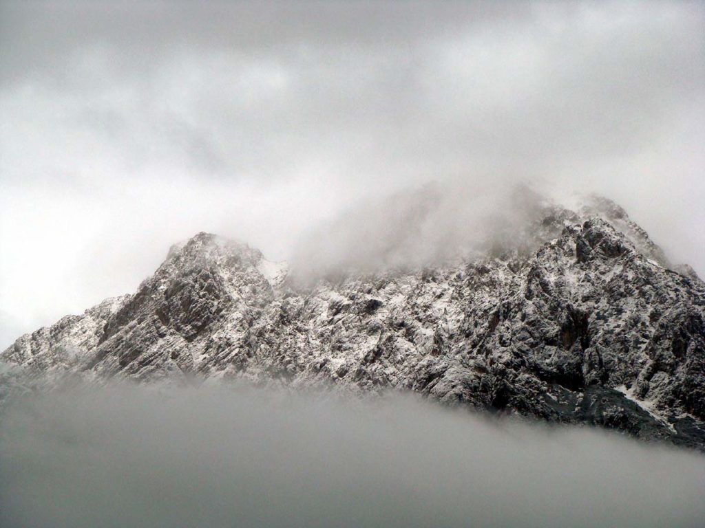 Il Crissin avvolto tra le nubi dopo una leggera nevicata; sulla destra appare la cima dello Schiavon sulla cui sommità si intuisce la croce di vetta